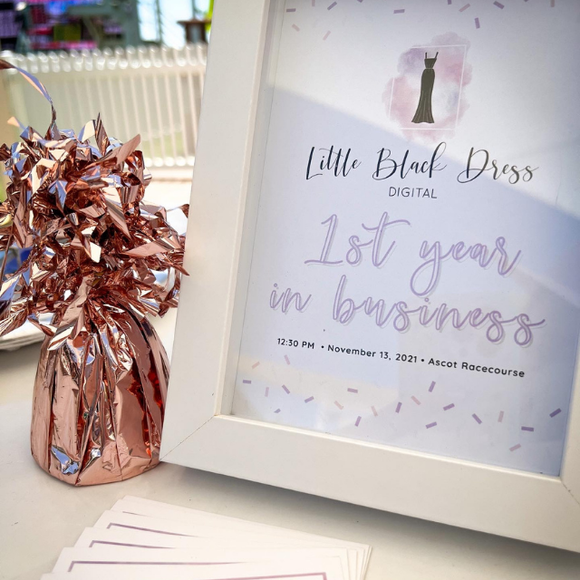 A graphic in a photo frame which reads “Little Black Dress Digital - 1st year in business”. Next to the frame is a rose gold table weight